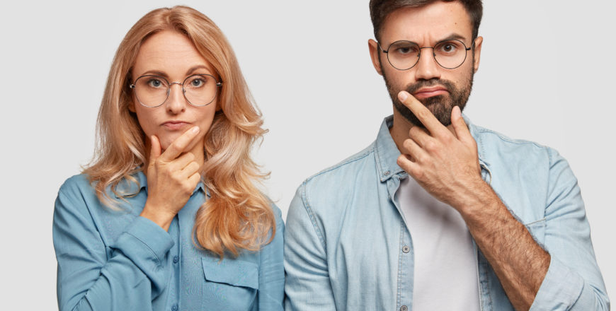 Horizontal shot of thoughtful male and female colleagues hold chins and being concentrated on solving problem, look directly into camera. Blonde middle aged female and her brother work as team